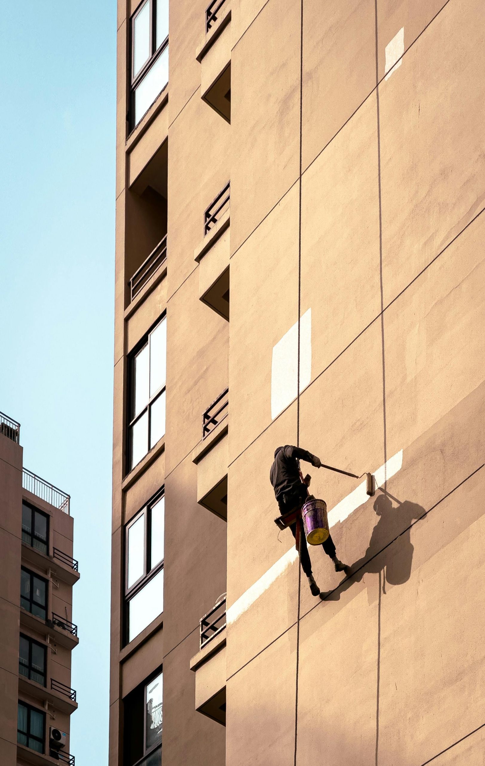 Trabajador en altura pintando una fachada de gran altura con rodillo.