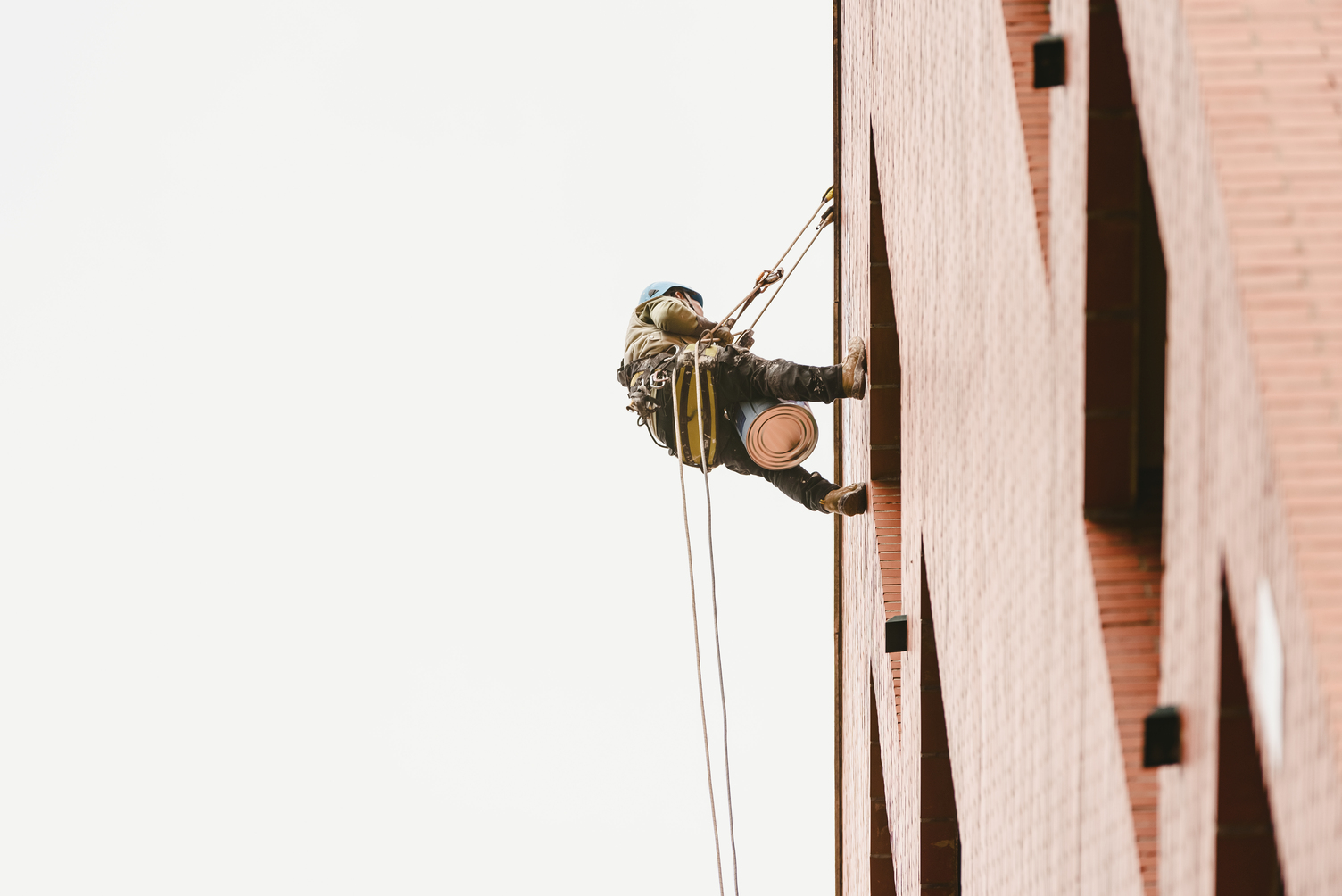 Técnico de trabajos verticales aplicando impermeabilización en la fachada de un edificio.