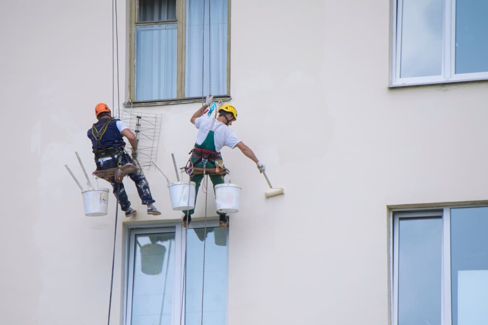 Pintores especializados aplicando revestimiento en una fachada de gran altura.